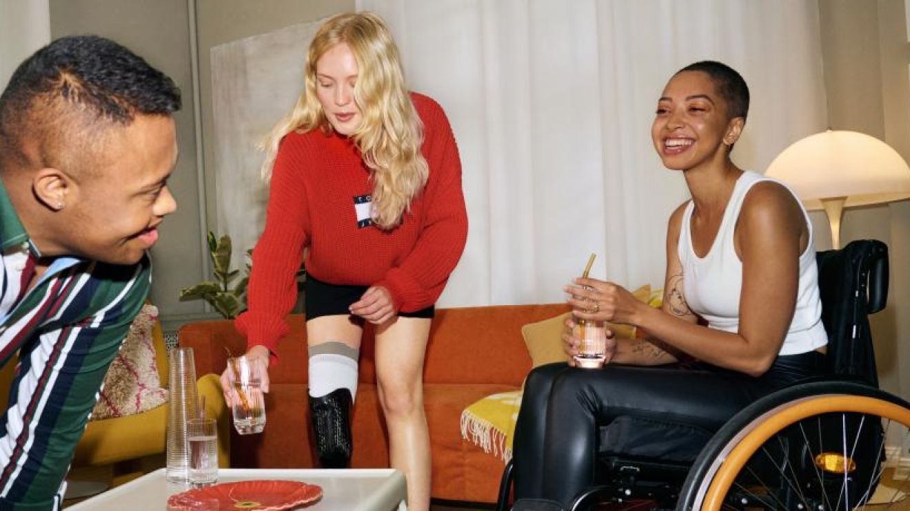 Three disabled models laugh together around a coffee table.
